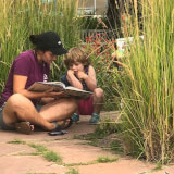 a volunteer reading to a child on the ground surrounded by tall grasses